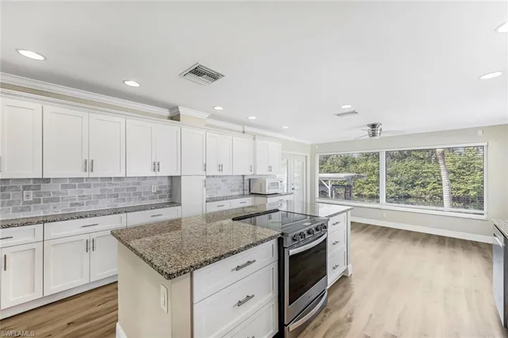 Kitchen with decorative backsplash, white cabinetry, stainless steel range with electric cooktop, and stone counters