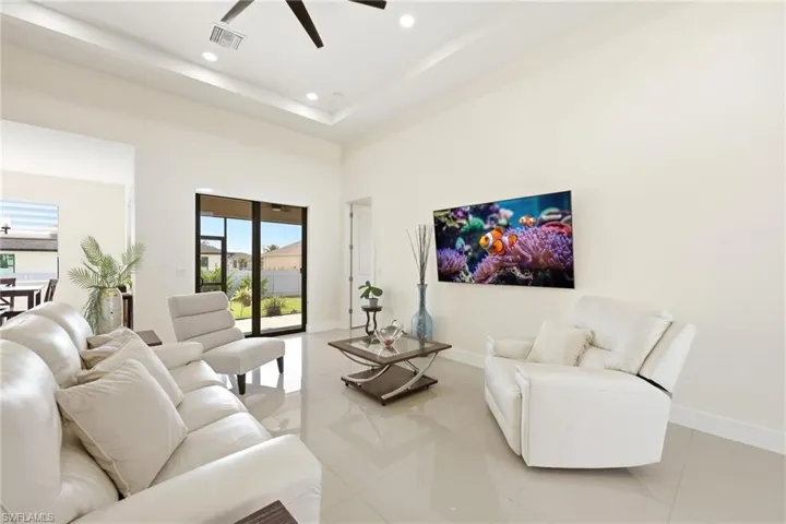 Living area featuring ceiling fan, light tile patterned flooring, a raised ceiling, and recessed lighting