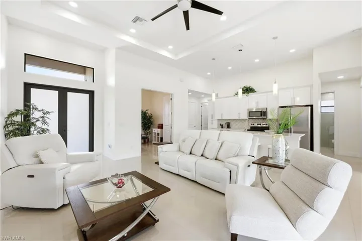 Living room featuring a tray ceiling, healthy amount of natural light, a ceiling fan, recessed lighting, and light tile patterned floors