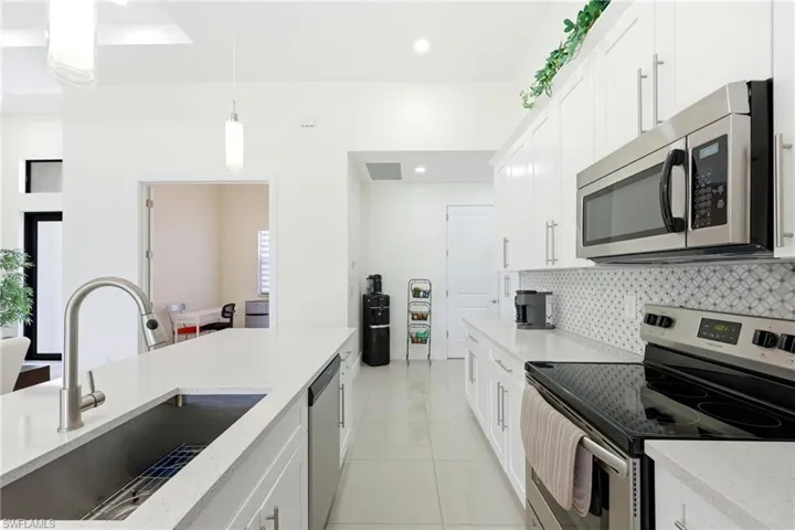 Kitchen featuring stainless steel appliances, white cabinetry, light stone counters, light tile patterned flooring, and pendant lighting