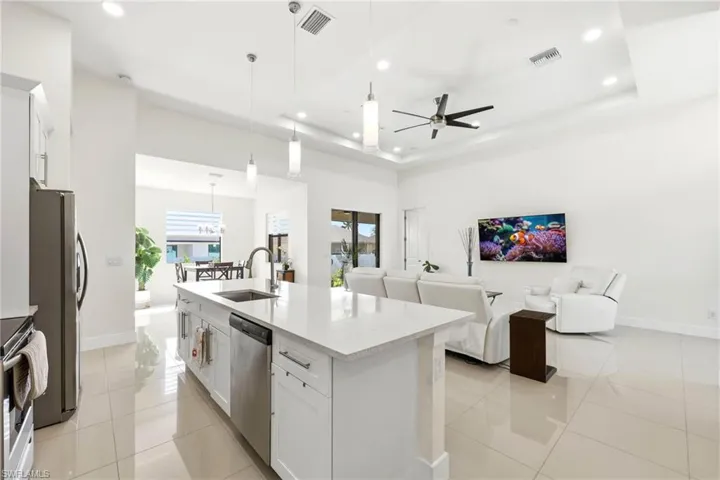 Kitchen featuring white cabinets, open floor plan, decorative light fixtures, light stone countertops, and a kitchen island with sink