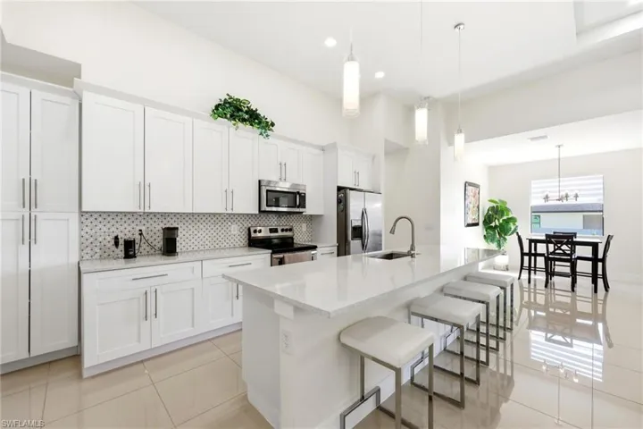 Kitchen featuring light tile patterned flooring, hanging light fixtures, white cabinetry, stainless steel appliances, and a kitchen island with sink