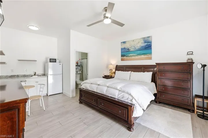Bedroom with freestanding refrigerator, a ceiling fan, light wood-style floors, and ensuite bath