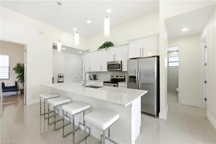 Kitchen with stainless steel appliances, a kitchen breakfast bar, white cabinetry, and light tile patterned floors