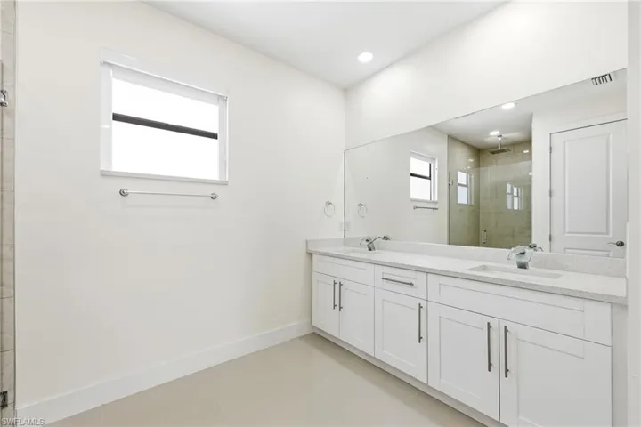 Bathroom featuring double vanity, light tile patterned floors, a shower stall, and recessed lighting