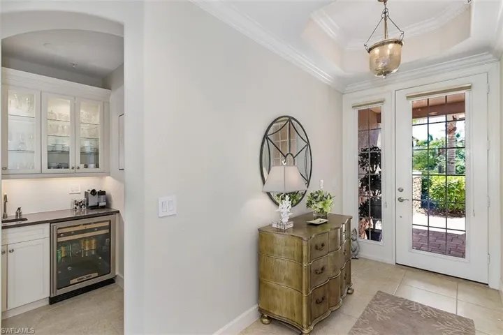 Tiled entryway featuring indoor wet bar, beverage cooler, a raised ceiling, and crown molding