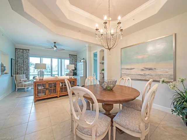 Tiled dining area featuring crown molding, ceiling fan with notable chandelier, and a tray ceiling