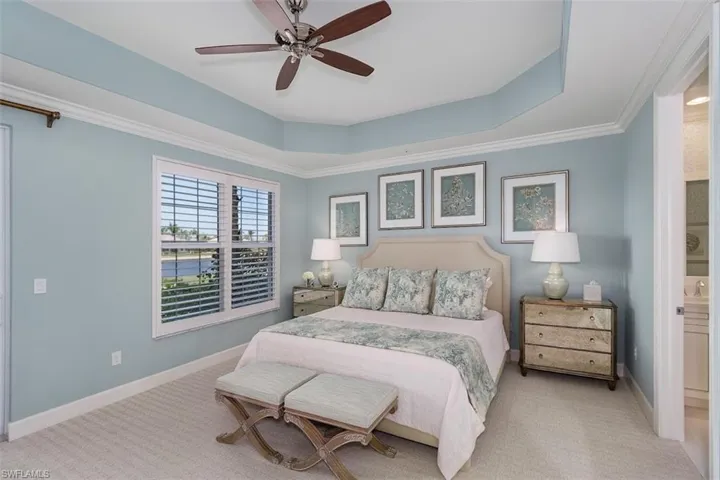Carpeted bedroom with a tray ceiling, ornamental molding, ceiling fan, and ensuite bathroom