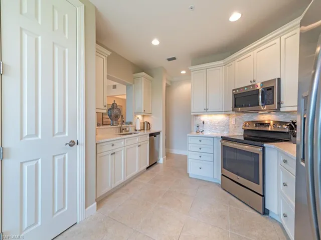 Kitchen featuring decorative backsplash, white cabinets, light stone countertops, light tile patterned floors, and stainless steel appliances