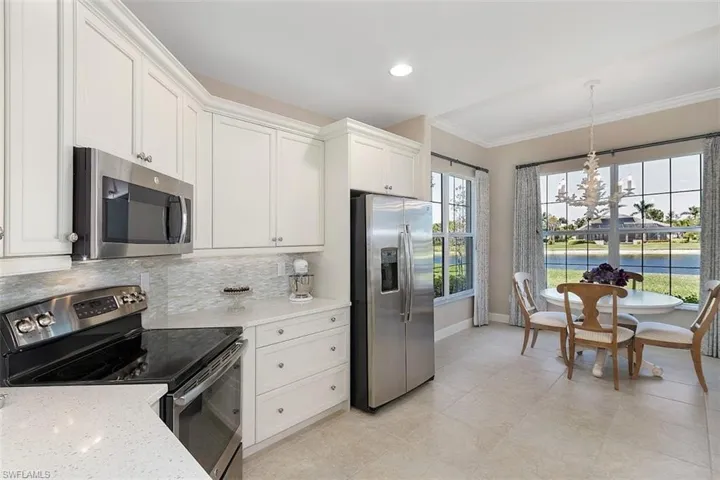 Kitchen with appliances with stainless steel finishes, hanging light fixtures, white cabinetry, light stone counters, and ornamental molding