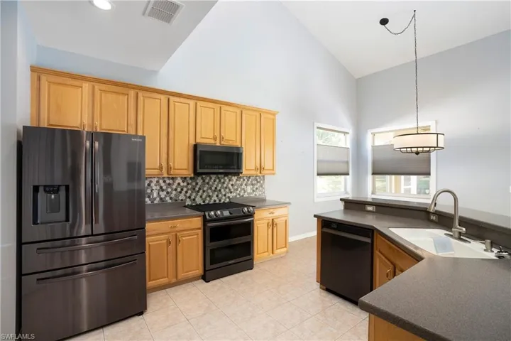 Kitchen featuring dark countertops, black appliances, high vaulted ceiling, decorative light fixtures, and decorative backsplash
