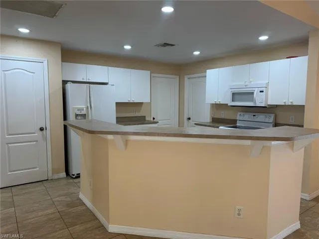 Kitchen featuring white cabinets, visible vents, a breakfast bar, and white appliances