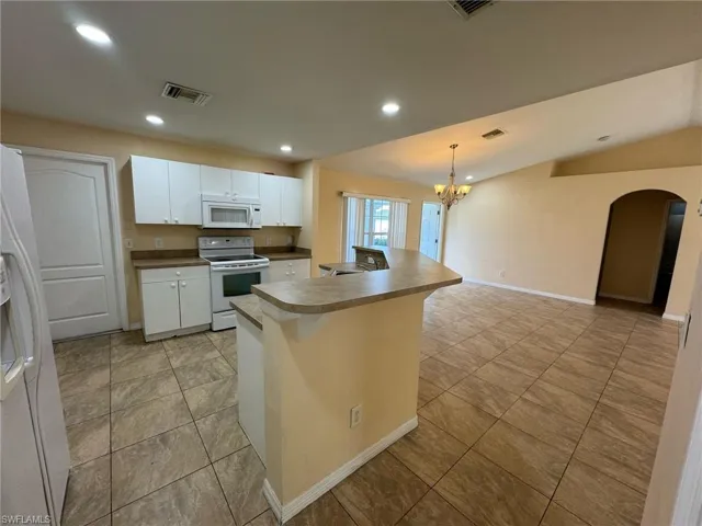Kitchen with white cabinetry, visible vents, an inviting chandelier, and white appliances