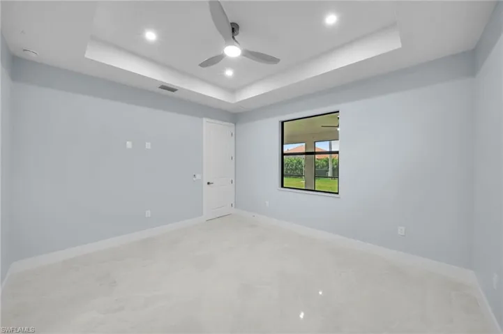 Empty room with visible vents, baseboards, ceiling fan, a tray ceiling, and recessed lighting