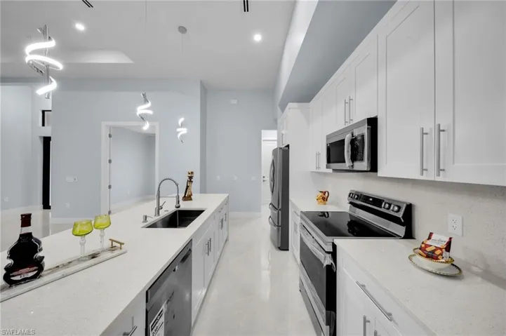 Kitchen featuring light stone counters, a sink, white cabinets, appliances with stainless steel finishes, and pendant lighting