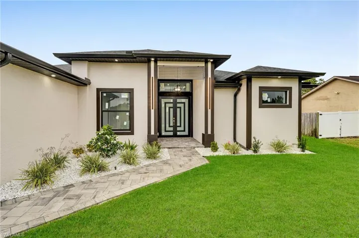 Doorway to property featuring stucco siding, a lawn, and fence