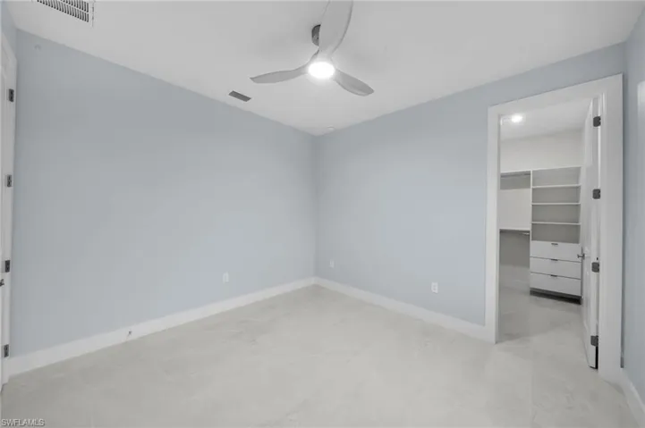 Unfurnished bedroom featuring a walk in closet, baseboards, visible vents, and ceiling fan