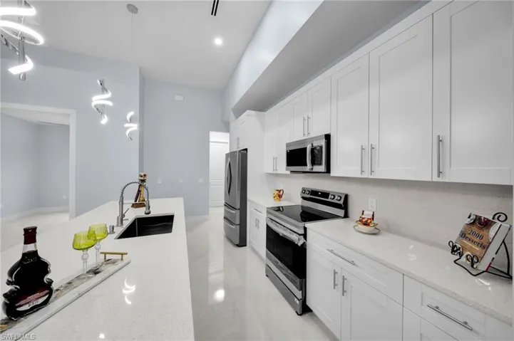 Kitchen featuring pendant lighting, a sink, stainless steel appliances, white cabinets, and light stone countertops