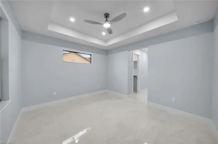 Unfurnished room featuring a raised ceiling, marble finish floor, a ceiling fan, recessed lighting, and baseboards