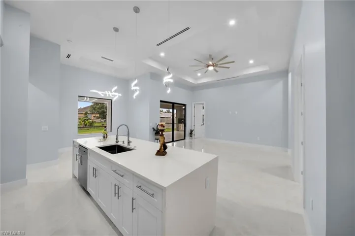 Kitchen with visible vents, an island with sink, a tray ceiling, white cabinetry, and a sink