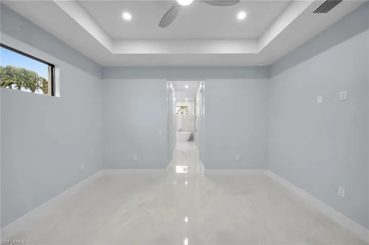 Empty room with a tray ceiling, baseboards, visible vents, and marble finish floor