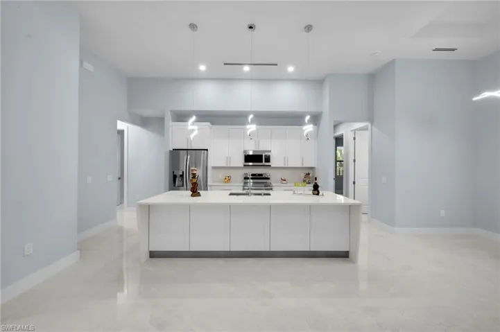 Kitchen featuring baseboards, light countertops, appliances with stainless steel finishes, a large island, and white cabinets