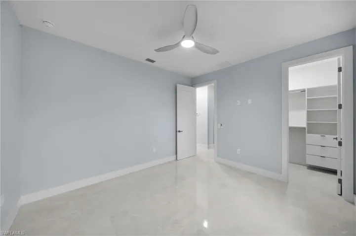 Unfurnished bedroom featuring a ceiling fan, visible vents, baseboards, a closet, and a walk in closet