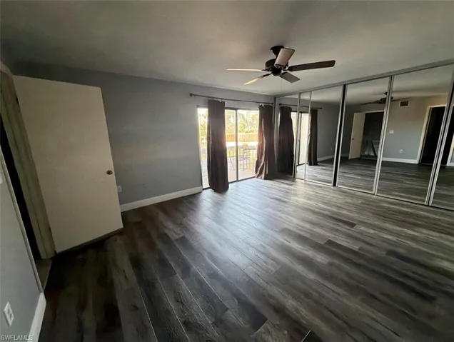 Unfurnished bedroom featuring access to exterior, dark wood-style flooring, and a ceiling fan