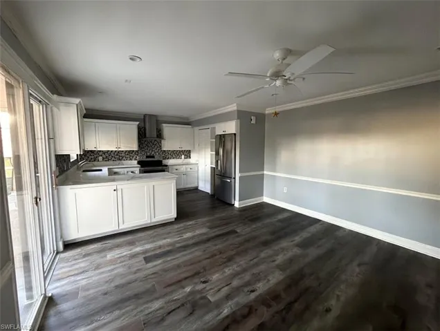 Kitchen with white cabinets, a peninsula, crown molding, wall chimney exhaust hood, and stainless steel appliances
