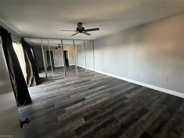 Unfurnished bedroom featuring a closet, dark wood-style flooring, and a ceiling fan