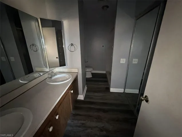 Full bath featuring double vanity and dark wood finished floors