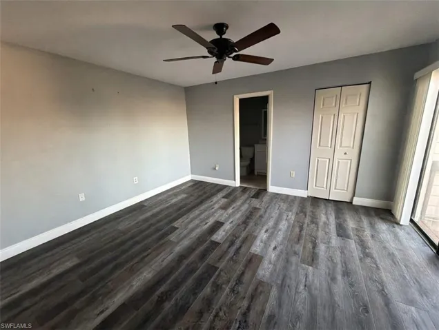 Unfurnished bedroom featuring dark wood-style floors, a closet, a ceiling fan, and ensuite bath