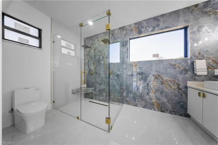 Full bathroom with healthy amount of natural light, vanity, a marble finish shower, and marble tiled flooring