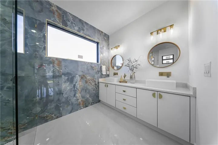 Bathroom featuring double vanity, a marble finish shower, and light marble finish floors