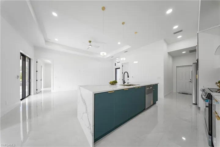 Kitchen with hanging light fixtures, a ceiling fan, a kitchen island with sink, electric stove, and a raised ceiling