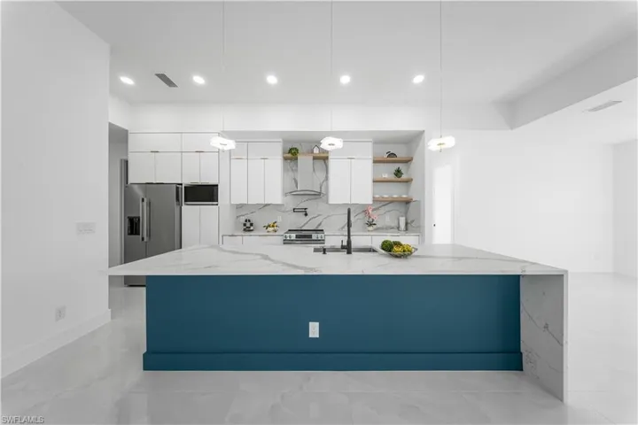 Kitchen with white cabinets, open shelves, light stone countertops, appliances with stainless steel finishes, and backsplash