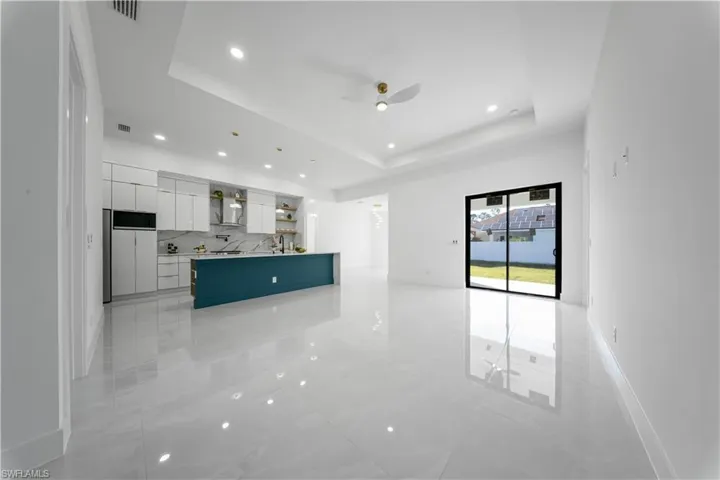 Unfurnished living room featuring recessed lighting, ceiling fan, a tray ceiling, and light marble finish floors