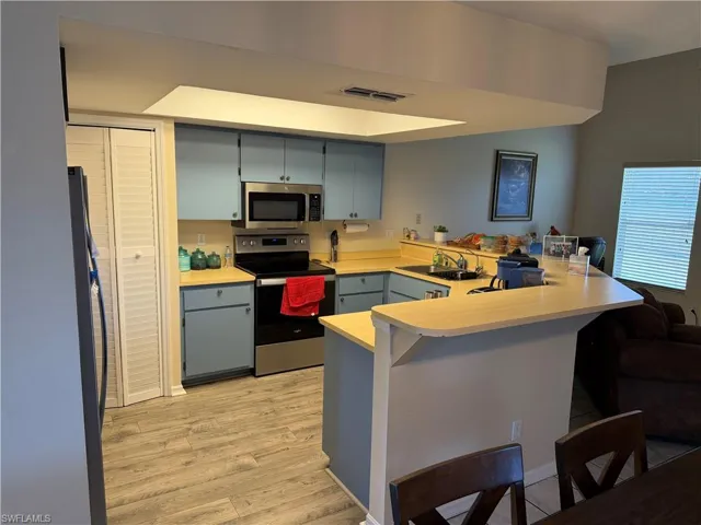 Kitchen featuring a peninsula, stainless steel appliances, light countertops, light wood-style flooring, and a breakfast bar