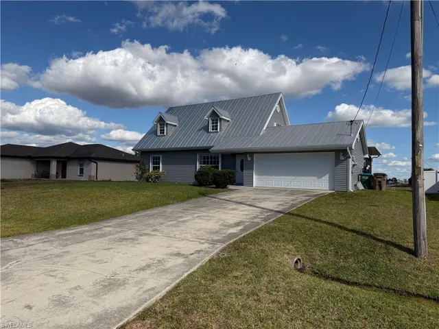View of front facade featuring a garage, a front lawn, concrete driveway, and a metal roof