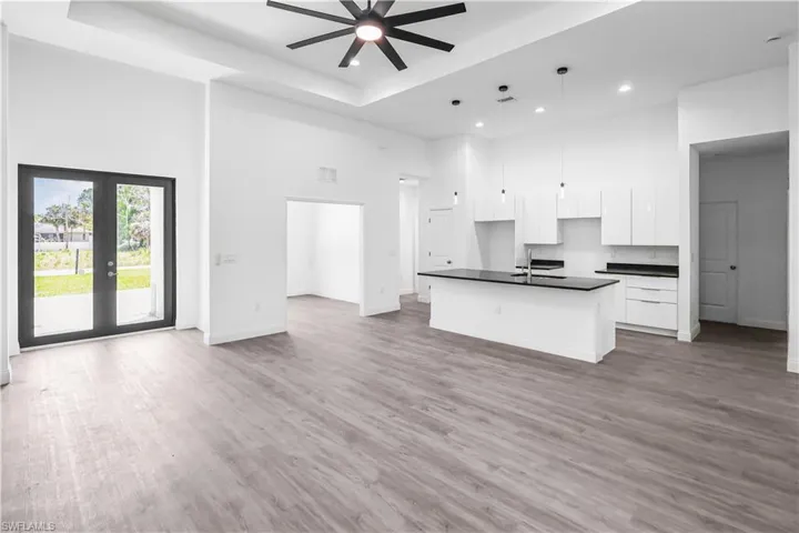 Kitchen with a high ceiling, dark countertops, white cabinetry, an island with sink, and open floor plan