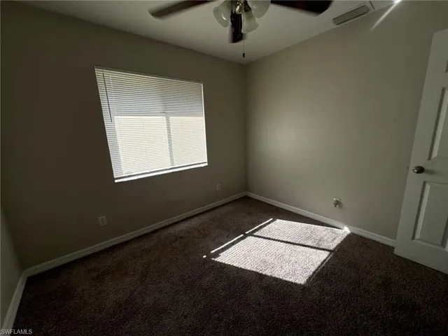 Unfurnished room with ceiling fan and dark carpet