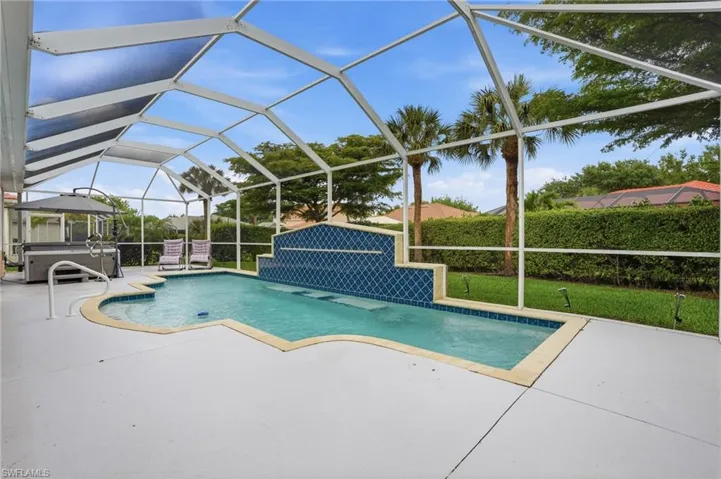The screened-in patio features a swimming pool with a decorative tiled waterfall, a hot tub, and ample deck space for relaxation