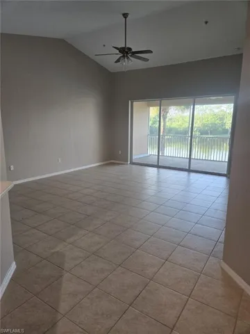 Tiled empty room with vaulted ceiling and a ceiling fan