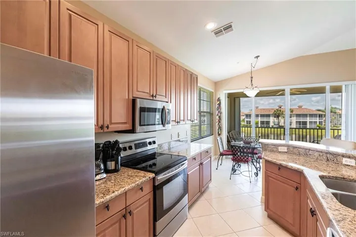 Kitchen featuring appliances with stainless steel finishes, vaulted ceiling, light stone countertops, light tile patterned floors, and decorative light fixtures