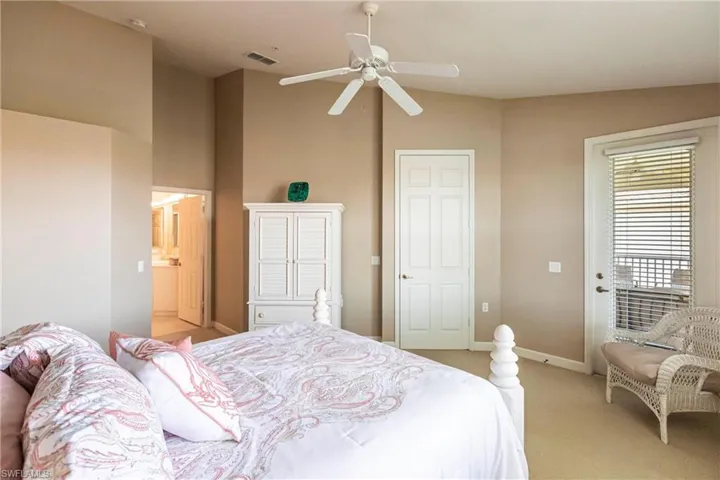 Carpeted bedroom featuring ceiling fan, ensuite bathroom, and high vaulted ceiling