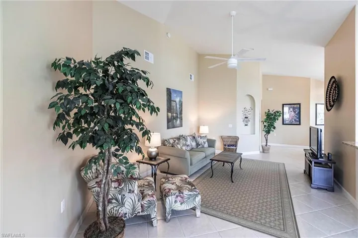Living room with light tile patterned flooring, arched walkways, a ceiling fan, and a high ceiling