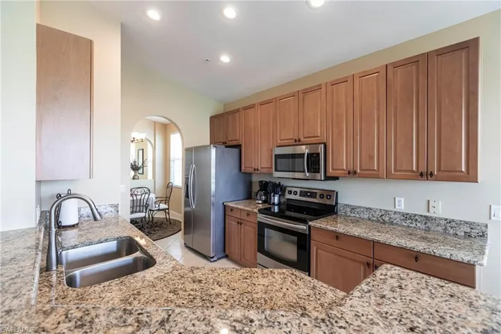 Kitchen featuring brown cabinets, appliances with stainless steel finishes, arched walkways, light stone countertops, and light tile patterned floors
