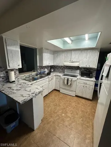 Kitchen with electric range, freestanding refrigerator, light countertops, backsplash, and a peninsula