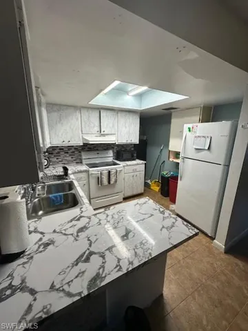 Kitchen featuring white appliances, a skylight, light countertops, a peninsula, and tile patterned floors