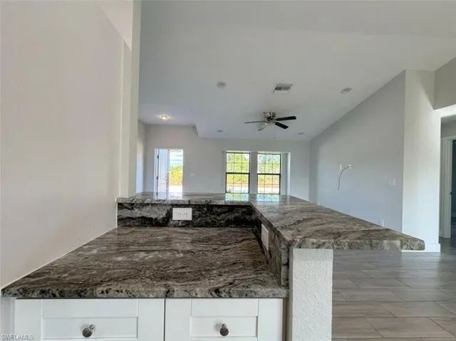 Kitchen featuring dark stone counters, a ceiling fan, white cabinets, open floor plan, and recessed lighting